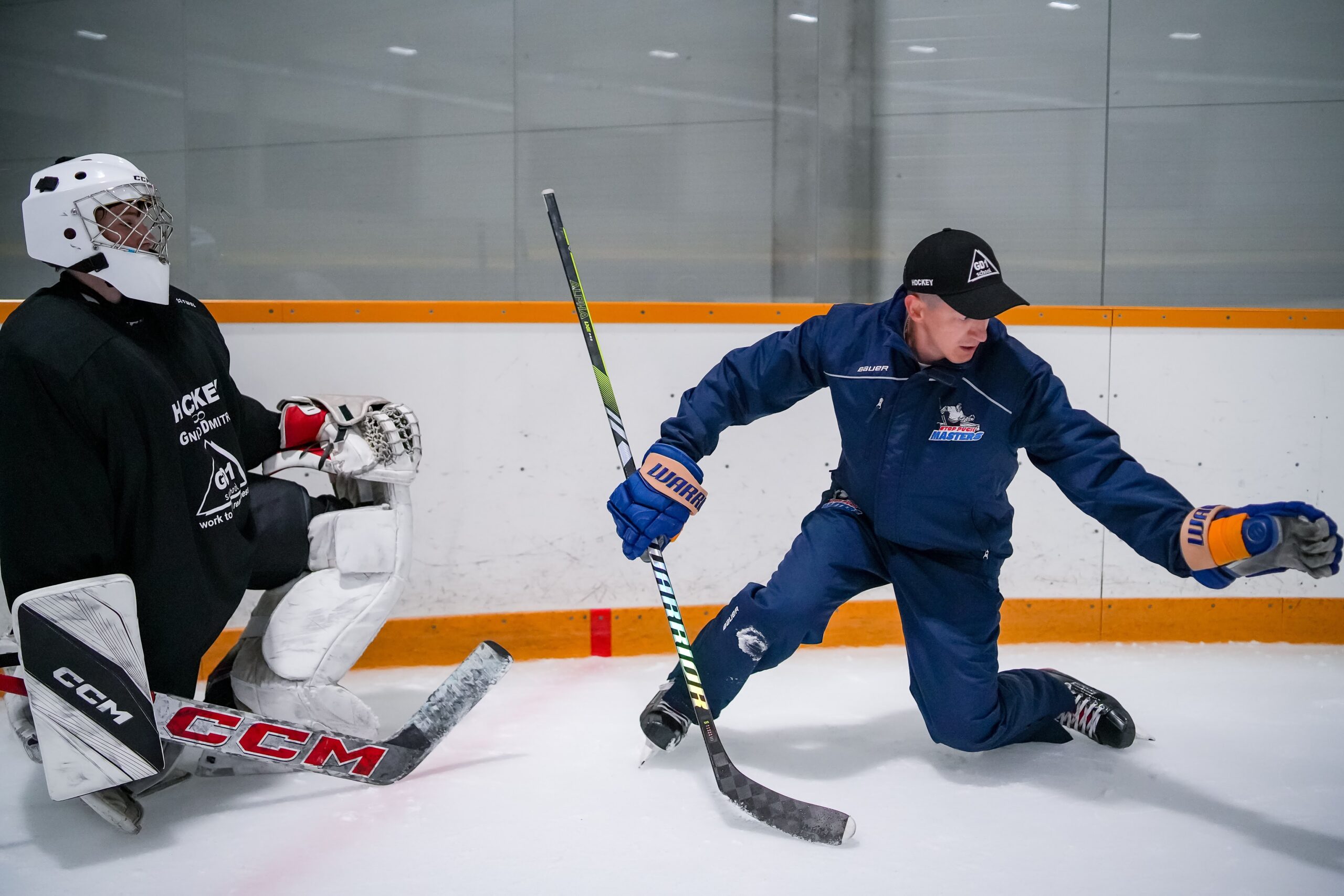A coach working with a goalkeeper on the ice